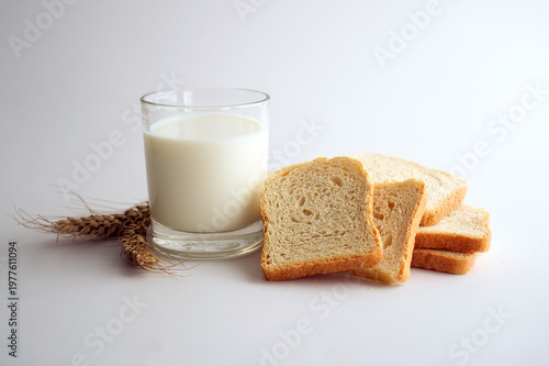 Glass of fresh milk with bread slices and wheat on white background.