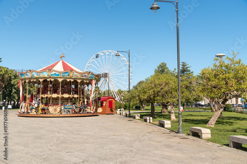Wallpaper Mural Carousel in Piazza Crispi with a Ferris wheel in the background in the center of Olbia, Sardinia, Italy. Festive amusement attraction in a city square. Torontodigital.ca