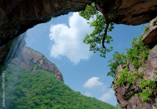 Upward waterfall cave opening blue sky green cliff rock arch mountain view cloud copy space