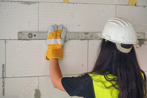 Female construction worker checking white aac bricks with horizontal level, view form behind, face not visible