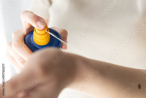 Closeup of a woman applying spray sunscreen.