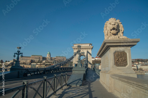 Famous stone lion statue at the entrance of Szechenyi Chain Bridge with Buda Castle in the background.