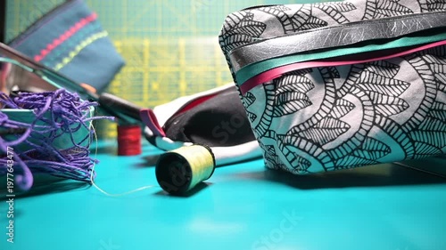 Conceptual video showing colorful sewing pouches of different sizes arranged on a patchwork mat, with a spool of thread moving across the scene. Creative and artistic atmosphere representing handmade 