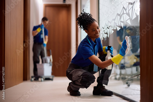 Photos Black janitorial service employee polishing glass surface in office building