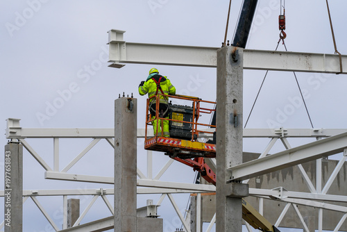Photos Construction worker installing steel beams from lift platform on industrial buil