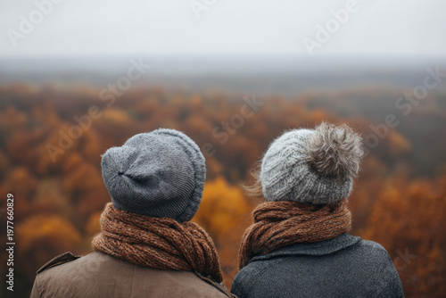 A loving couple in cozy sweaters enjoys a serene autumn day outside their countryside house, surrounded by bright yellow and red foliage. Togetherness and slow lifestyle. Back view photo.