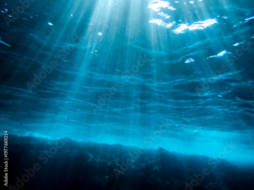 Ocean blue underwater with sunrays, Underwater Sea Deep Water Abstract Sunshine, sea wave , clean waters in summer time, Natural underwater seascape, sand on ocean floor and water surface sunlight.