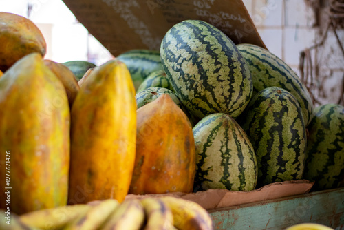 Fresh tropical fruits on a wooden stand at a vegetable market. Large, oblong papayas with yellow-orange skin are juicy and delicious. Watermelons of various sizes. Selective focus.