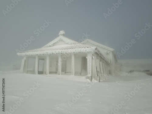 View of a building encased in thick ice stands starkly against the desolate, snow-covered landscape, a testament to winter's harsh grip, Covilha, Distrito da Guarda, Portugal.