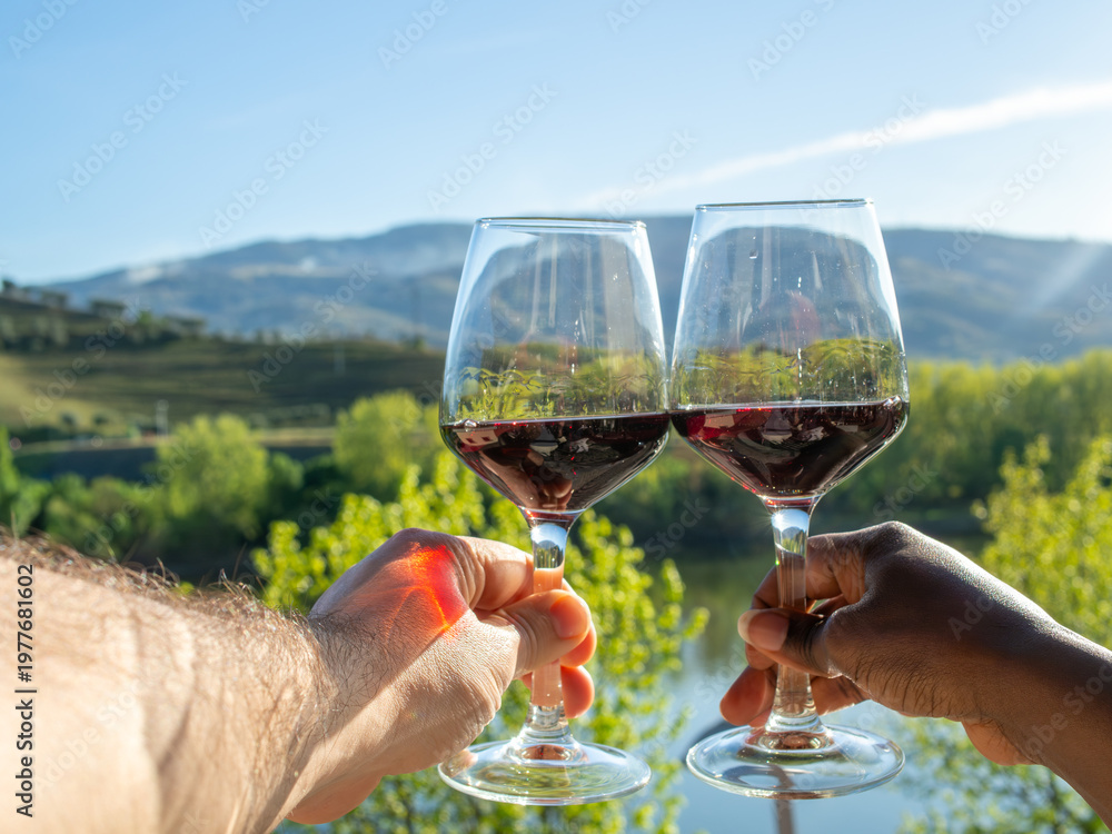 Fototapeta premium Close Up of Hands Clinking Wine Glasses in Peso da Régua with Sunlit Douro Valley Mountains Behind
