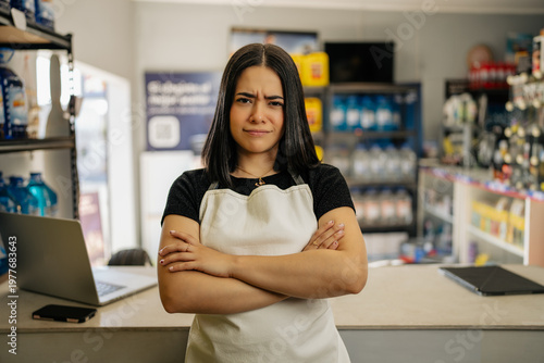 Konstfotografi Young woman employee in apron with crossed arms showing an annoyed face