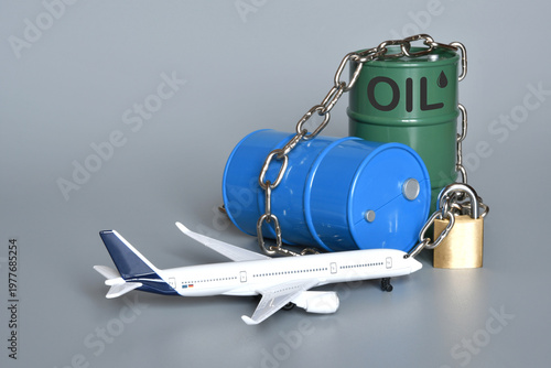 Miniature oil barrels locked with a chain and padlock, along with an airplane. Concept of the shortage and rising price of jet fuel due to the Middle East crisis and the war in Iran.