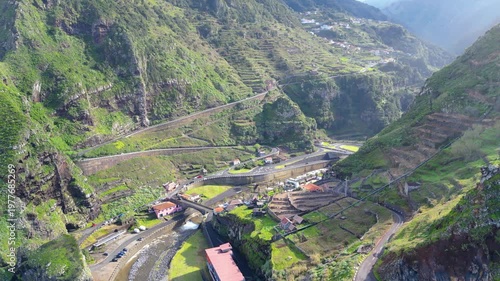 Aerial view of Madeira's stunning Ribeira da Janela valley, showcasing winding roads, lush green terraces, and a river under the late afternoon sun. A breathtaking landscape of human ingenuity and nat