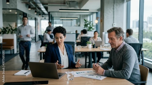 Medium shot of a broker consulting an individual investor in a sleek openplan office softly blurred colleagues working in the background