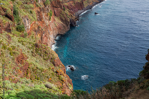 Steep rocky cliffs above deep blue ocean with clear water below. Rugged coastline with natural textures and vibrant colors