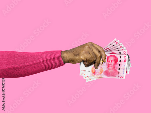 A person in a pink sweater holds a fanned-out stack of 100-Yuan Chinese Renminbi notes against a solid pink background. The image represents finance, investment, and global trade