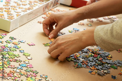 A woman is assembling puzzles at home in natural light. Only hands are visible.