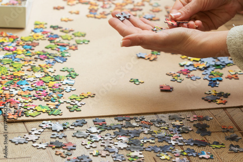 A woman is assembling puzzles at home in natural light. Only hands are visible.
