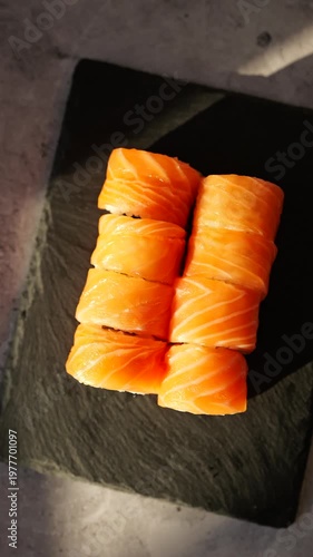 Fresh salmon sushi rolls are beautifully displayed on a dark slate plate, showcasing their rich orange hue