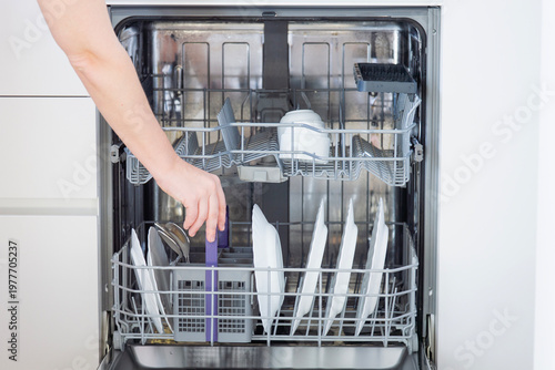 Canvas-taulu a person reaching out to take a grey cutlery basket from an open dishwasher fill