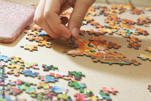 A teenage girl is putting together a puzzle. Only her hands are visible.