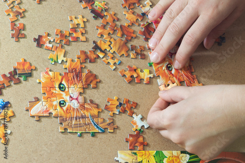 A teenage girl is putting together a puzzle. Only her hands are visible.