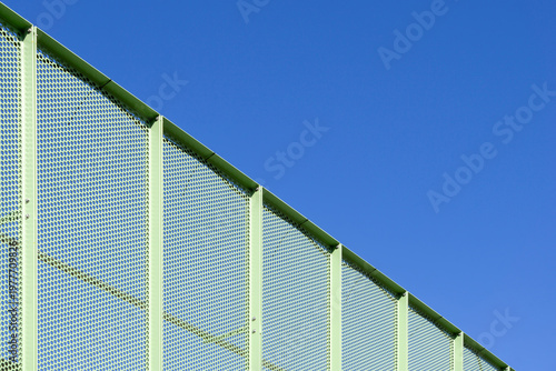 Modern Green Perforated Metal Architectural Screen Against Clear Blue Sky