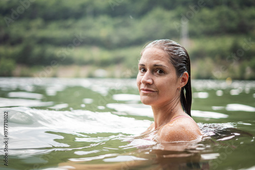A serene woman enjoying a refreshing swim in a natural lake surrounded by lush greenery