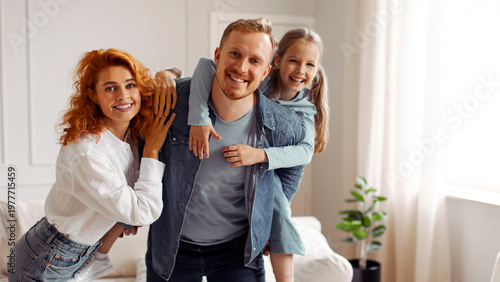 Φωτογραφία Happy European parents and their daughter posing at home, girl piggybacking fath