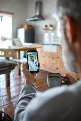 Senior man consulting doctor on smartphone in home kitchen