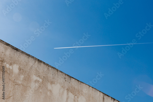 Foto A minimalist view looking up at the angled edge of a weathered concrete wall against a clear blue sky featuring a single white vapor trail
