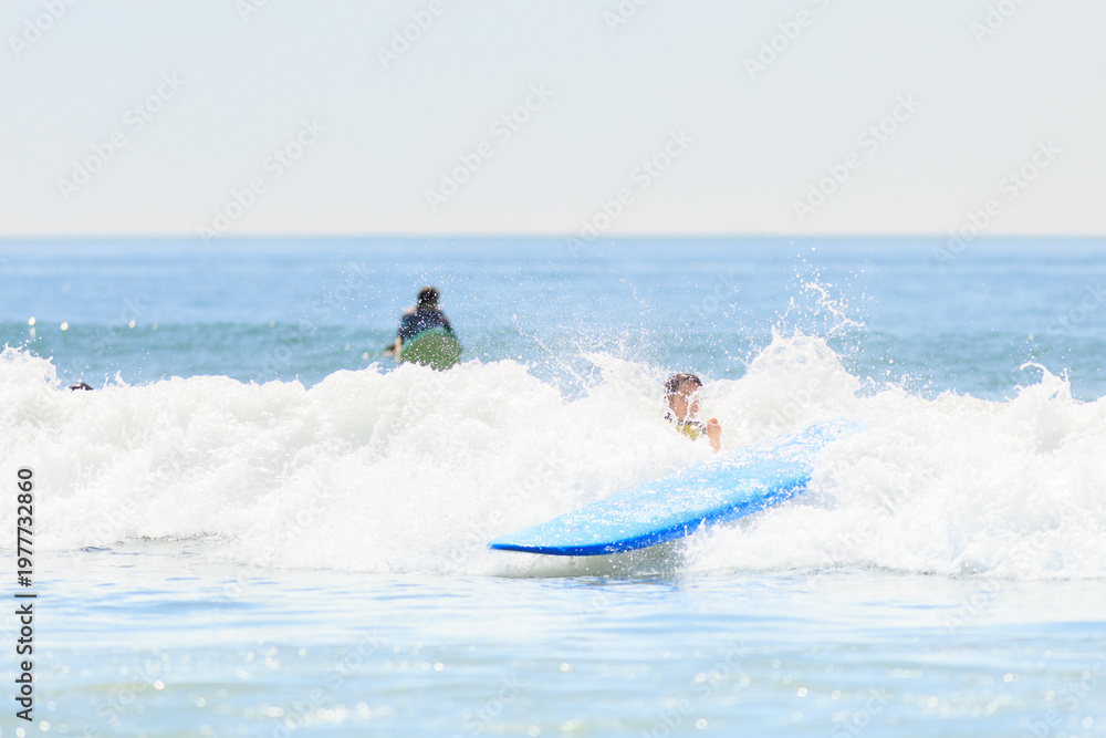 Obraz premium A surfer falls into the ocean as their blue surfboard splashes through a wave, capturing an action-packed surfing wipeout moment. Stock photo