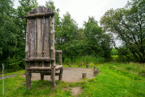Big wooden chair made of boards and logs at Cuningar Loop woodland park in Glasgow. Scotland. Rustic large wooden armchair. In park  walking trails, boardwalk, a woodland meadow loop, riverside paths.