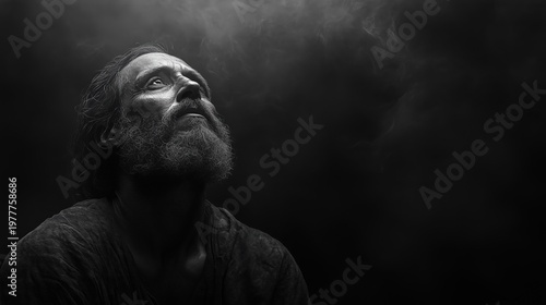 A man with a beard and long hair looks up at something in a dark and moody atmosphere with smoke around him