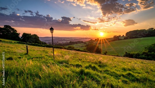 Golden hour view sun rays over green field, trees, and distant structures