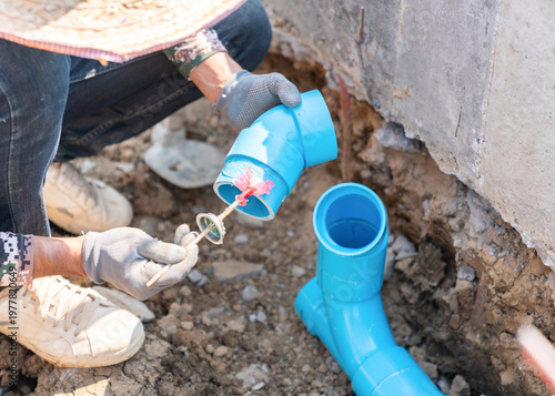 Close-up of a worker bonding plastic water pipes with adhesive at a construction site.