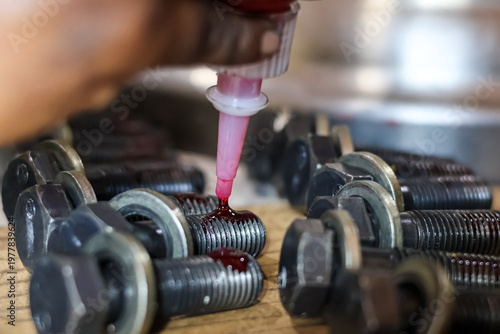Technician applying red threadlocker adhesive to heavy duty bolt threads during industrial workshop assembly.