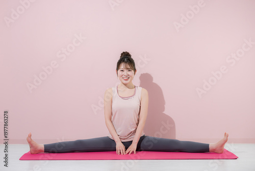 Foto ピンク背景開脚前屈で柔軟性を高める女性のヨガとストレッチの基本ポーズイメージ全身カメラ目線の笑顔