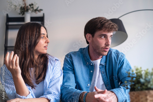 Schilderij op canvas A young couple sits in their living room during a tense conversation, showing disagreement, frustration and emotional distance as they struggle with communication and relationship conflict at home