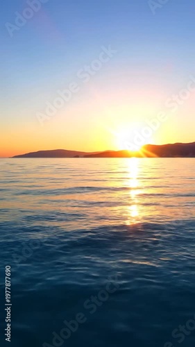 A serene view of the calm ocean water reflecting the warm golden light of a beautiful sunset over distant rolling hills