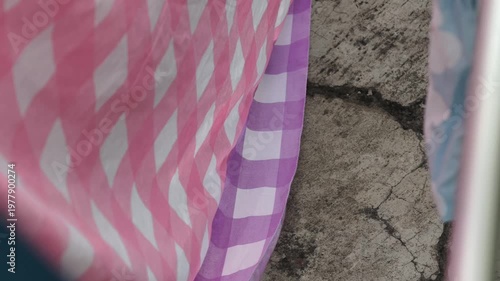 Close up of Pink and Purple Gingham Fabric Gently Blowing in the Wind Against a Textured Wall