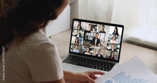 Картината върху платно Businesswoman engages in virtual meeting with diverse group displayed on laptop screen, view over her shoulder