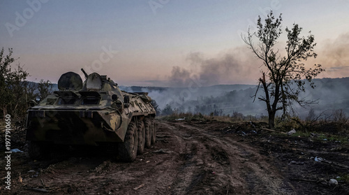 Tableau sur toile Armored personnel carrier on a dirt road at dusk, overlooking a smoky, war-affected landscape with hills