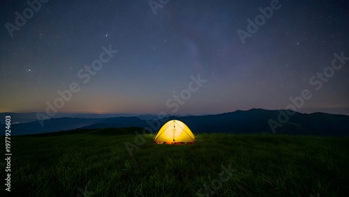 Nighttime mountain view featuring illuminated tent under starry sky with long exposure effect