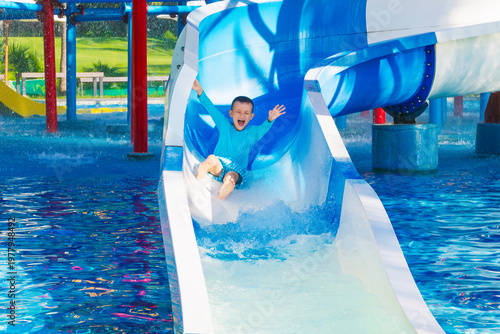 happy funny child boy rides a water slide in a water park in summer vacation. Children's aquapark in swimming pool at the resort