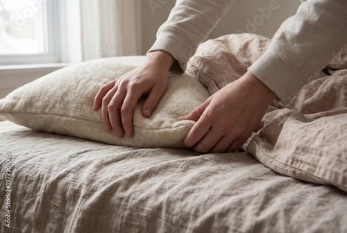 Woman's hands adjusting a comfortable pillow on a neutral colored bed