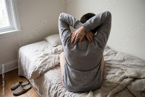 Woman in grey sweatshirt stretching on bed in the morning