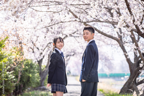桜の下で振り返る制服を着たふたりの生徒