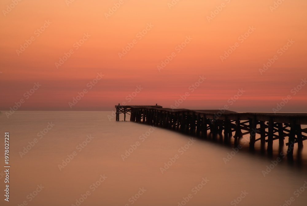 Fototapeta premium Wooden jetty at sunset in Alcudia Bay, Mallorca, Spain. Long exposure of Playa de Muro beach, minimalist zen concept with calm water and negative space