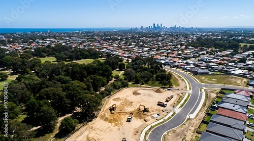 New housing estate construction in a Melbourne suburb with heavy machinery, surrounding residential neighborhoods, and a coastal city background